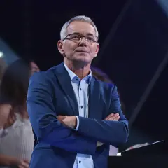 Robert Janowski w garniturze, z rękami skrzyżowanymi na piersi, na tle sceny. Czy to właśnie powód, dlaczego Robert Janowski naprawdę odszedł z Jaka to melodia po latach?