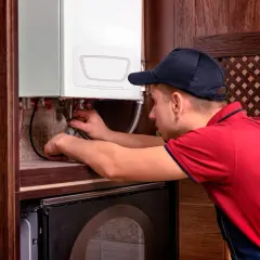 Fachowiec w czerwonej koszulce i granatowym ogrodniczkach wykonuje serwis pieców gazowych Brotje, pracując przy instalacji.
