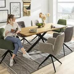 Frau liest Magazin am breiten Esstisch mit modernen Stühlen und Blumen.