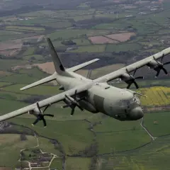 Potężny hercules samolot transportowy leci nad zielonymi polami i domami.