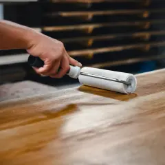 Main d'artisan appliquant un vernis sur un plateau en bois avec un rouleau, étape clé pour savoir comment vitrifier une table en bois.