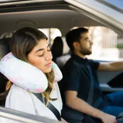 Donna dorme in auto con un cuscino cervicale fai da te, mentre l'uomo guida.