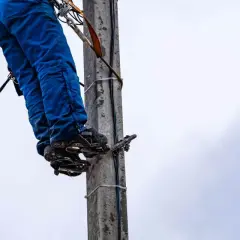 Energetyka chce zakopać kabel na mojej działce. Pracownik na słupie w niebieskich spodniach i z przyrządami.