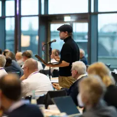 Mann mit Schirmmütze spricht bei der ekd synode ins Mikrofon, während Zuhörer aufmerksam folgen.
