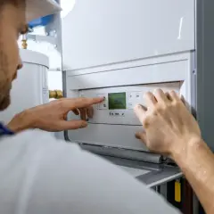 Fachowiec reguluje nowoczesną instalację gazową w domu. Na wyświetlaczu kotła widoczna jest temperatura 30.0.