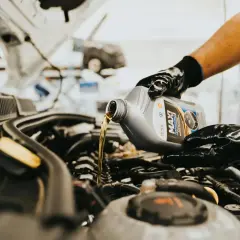 Main d'un mécanicien versant de l'huile neuve dans le moteur d'une voiture. C'est une étape clé de la vidange voiture, c'est quoi l'entretien moteur.