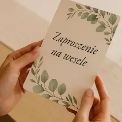 Dłonie trzymają zaproszenie na wesele z motywem liści. Warto wiedzieć, jak wypisać zaproszenia ślubne z osobą towarzyszącą i dzieckiem.