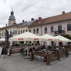 Letni ogródek kawiarniany na rynku w Żywcu. Parasole z logo Żywiec, stoliki i ławki. W tle kamienice i wieża ratuszowa.