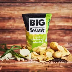 Reklamowa fotografia chipsów Big Snack o smaku zielonej cebulki, z ziemniakami i cebulką na drewnianym tle.