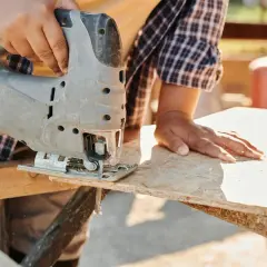 Ręce majsterkowicza tną płytę OSB wyrzynarką. Różne grubości płyt OSB pozwalają na wszechstronne zastosowanie.