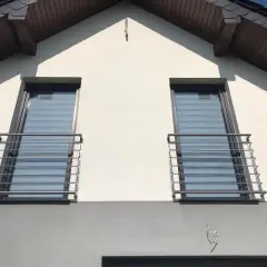Dwa nowoczesne portfenetry z metalowymi balustradami na białej elewacji domu.