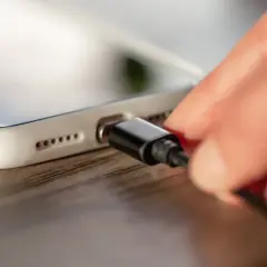 Dłoń podłącza kabel do białego smartfona. Zastanawiasz się, ile wynosi gwarancja na to urządzenie?
