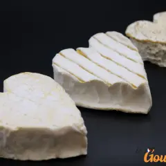 Trois fromages Neufchâtel en forme de cœur, dont un avec des stries, sur fond noir.