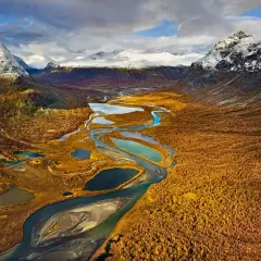 Herbstliche Farben im Tal mit Fluss und Seen, ideal für fernwanderwege schweden. Schneebedeckte Berge im Hintergrund.