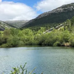 Un río serpentea entre montañas verdes y frondosos árboles. El cielo azul con nubes blancas corona el paisaje, invitando a recorrer sus gr 99 etapas.