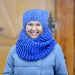 Uśmiechnięta kobieta w niebieskiej czapce i szaliku, idealny przykład, jak dobrać czapkę do płaszcza.