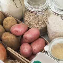 Kartoffeln lagern ohne Keller: Eine Kiste mit Kartoffeln und Zwiebeln neben Gläsern mit Reis und Haferflocken.