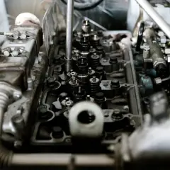 Wnętrze silnika z widocznymi zaworami i wtryskiwaczami. Słychać niepokojące klekotanie silnika, gdy mechanik pracuje nad jego naprawą.