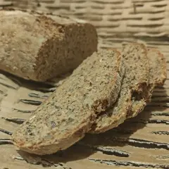 Chleb orkiszowy, pokrojony w kromki, z widocznymi ziarnami, leży na falistej tekturze.