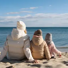 Rodzina w ciepłych ubraniach siedzi na plaży, patrząc na spokojne morze. Pogoda w czerwcu nad morzem bywa kapryśna, ale widok jest piękny.