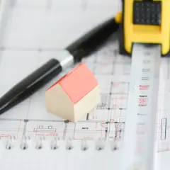 Miniaturowy domek, długopis i miarka na planach budowlanych. Zastanawiasz się, ile czasu jest ważne pozwolenie na budowę?