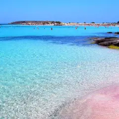 Niesamowita różowa plaża Kreta z krystalicznie czystą wodą i ludźmi kąpiącymi się w morzu.