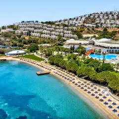 Widok na hotel Yasmin Bodrum Resort z plażą, basenami i białymi budynkami na wzgórzu. Idealne miejsce na wakacje, jak sugerują yasmin bodrum resort opinie.