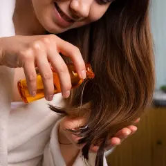 Mujer aplica aceite en su cabello. Descubre la vitamina e para que sirve en el cabello: brillo y fortaleza.