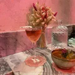 Un cocktail rose et un bol de fruits sur un marbre rose, ambiance douce et romantique d'un bisou bar.