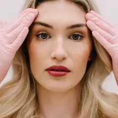 Kobieta w różowych rękawiczkach dotyka skroni, przygotowując się do zabiegu face lifting.
