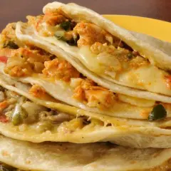 Quesadillas de pollo apiladas, rellenas de queso derretido y trozos de pollo sazonado, servidas en un plato amarillo con salsa al lado.