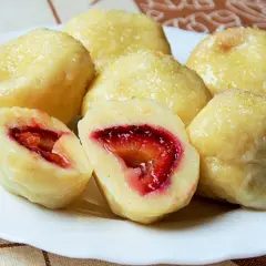 Pyszne, domowe knedle ze śliwkami, posypane cukrem, kuszą swoim wyglądem. Jedna z nich przekrojona na pół odsłania soczyste, czerwone wnętrze.