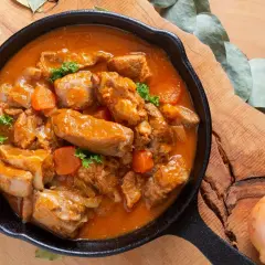 Gulasz z polędwiczki wieprzowej w aromatycznym sosie, z kawałkami marchewki i natki pietruszki, podany w żeliwnej patelni.