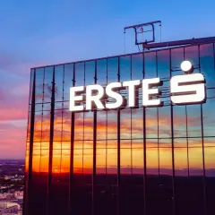 Zachód słońca nad miastem, odbijający się w szklanej fasadzie budynku z napisem "ERSTE S". Jak sprawdzić login w aplikacji Santander?