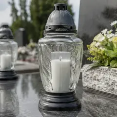 Zapalony znicz na kamiennym nagrobku, symbol pamięci i wiecznego światła. Obok bukiet białych kwiatów.