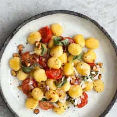 Pyszne makaron gnocchi z pomidorkami, szałwią i orzechami na talerzu.