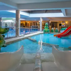Wesoły hotel z aquaparkiem zaprasza do zabawy! Dwa zielone dinozaury pilnują basenu ze zjeżdżalniami.