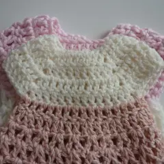 Crocheted baby dress in pink and white with openwork pattern.