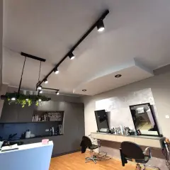 Nowoczesne oświetlenie salonu fryzjerskiego, z reflektorami na szynie i wiszącą lampą z roślinami, tworzy przytulną atmosferę.