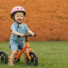 Uśmiechnięte dziecko w kasku na rowerku biegowym. Od jakiego wieku można zacząć naukę jazdy? Od ok. 18 miesiąca życia, gdy maluch pewnie stawia kroki.