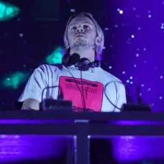 DJ na scenie, w słuchawkach na szyi, z napisem na koszulce. W tle niebieskie światła i efekty. To część lineupu Wisłoujście.