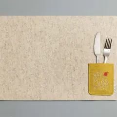 Beiges Platzset aus Filz mit gelber Tasche und der Aufschrift "Wer kleckert muss spülen!". Messer und Gabel stecken darin.