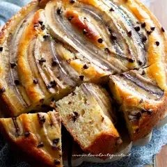 Delizioso dolce con banane e gocce di cioccolato, tagliato a fette su un tagliere di legno.