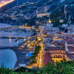 La **costiera amalfitana in moto** è un sogno al tramonto: luci accese sul porto e case aggrappate alla roccia.