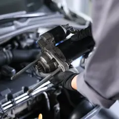 Mechanik w rękawiczkach trzyma rozrusznik. Zastanawiasz się, ile kosztuje wymiana rozrusznika?