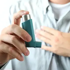 Dłoń trzymająca inhalator, druga ręka na piersi. To obraz walki z astmą, sensu stricto.