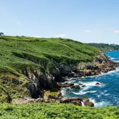 Sentier côtier verdoyant, le chemin des douaniers à Saint-Malo serpente le long de falaises rocheuses battues par la mer d'un bleu intense.