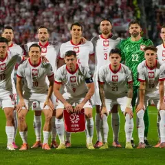 Zgrupowanie reprezentacji Polski. Piłkarze w białych strojach z orłem na piersiach pozują na tle trybun.