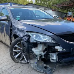 Uszkodzona Mazda na złomowisku, z urwanym zderzakiem i przebitą oponą. Może to być początek procesu, jak zezłomować samochód.