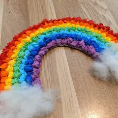 Ein bunter Regenbogen, gebastelt aus zerknülltem Krepppapier in allen Farben, mit flauschigen Wolken aus Watte.